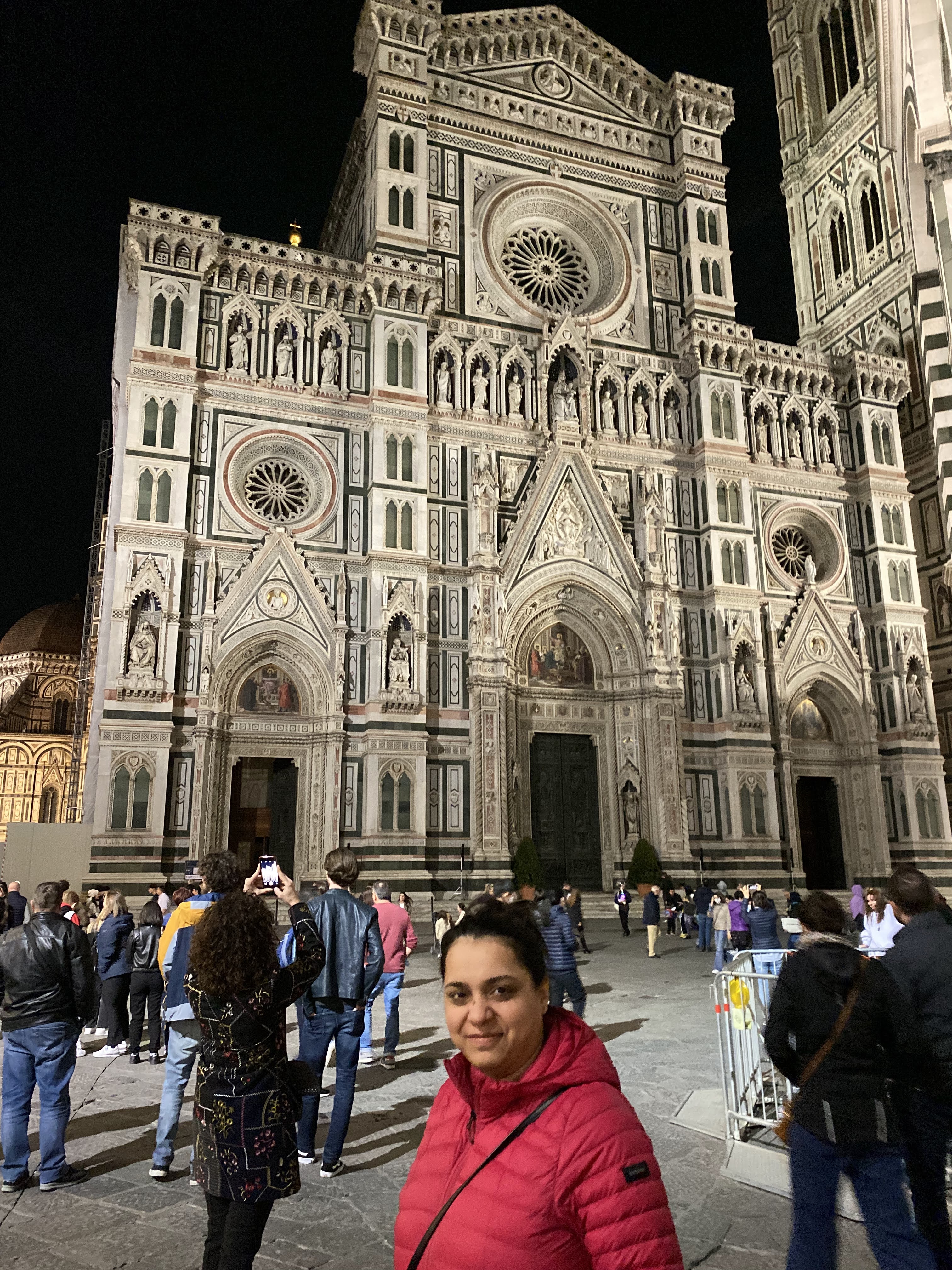 My wife standing in front of the illuminated Florence Duomo at night.