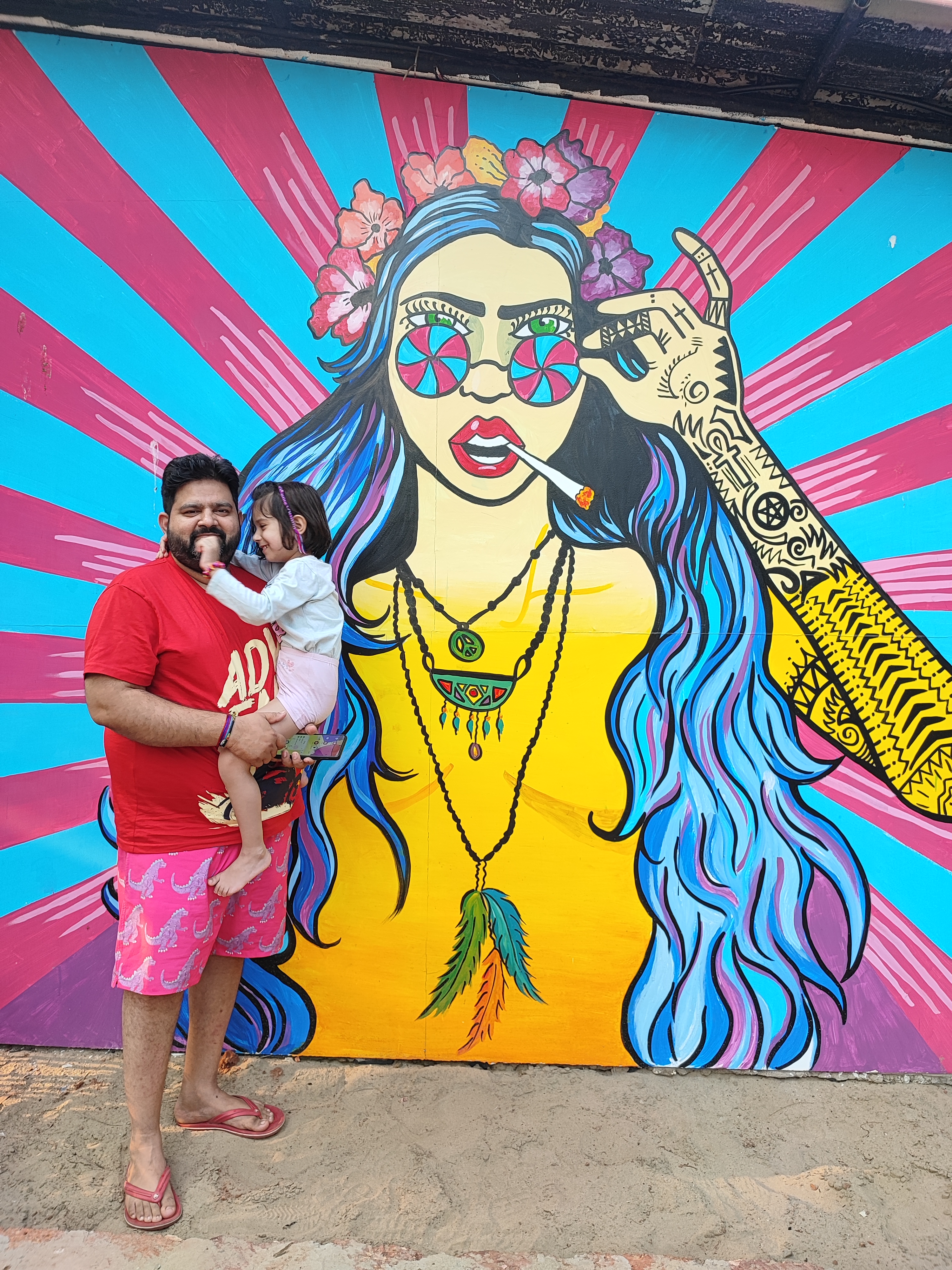 My husband holding our daughter in front of a vibrant Goa mural.