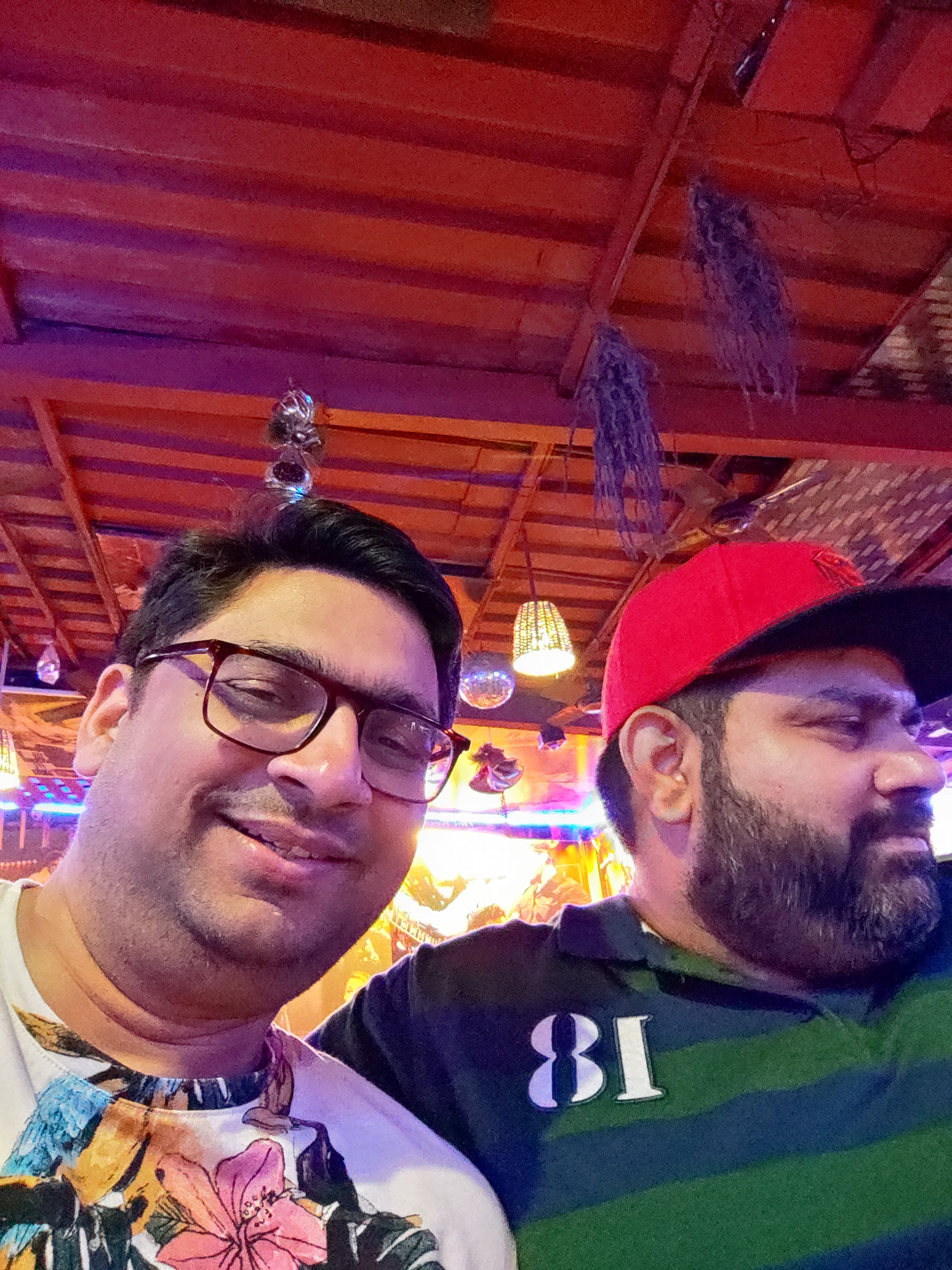 My husband and another man smiling in a lively Goan restaurant at night.