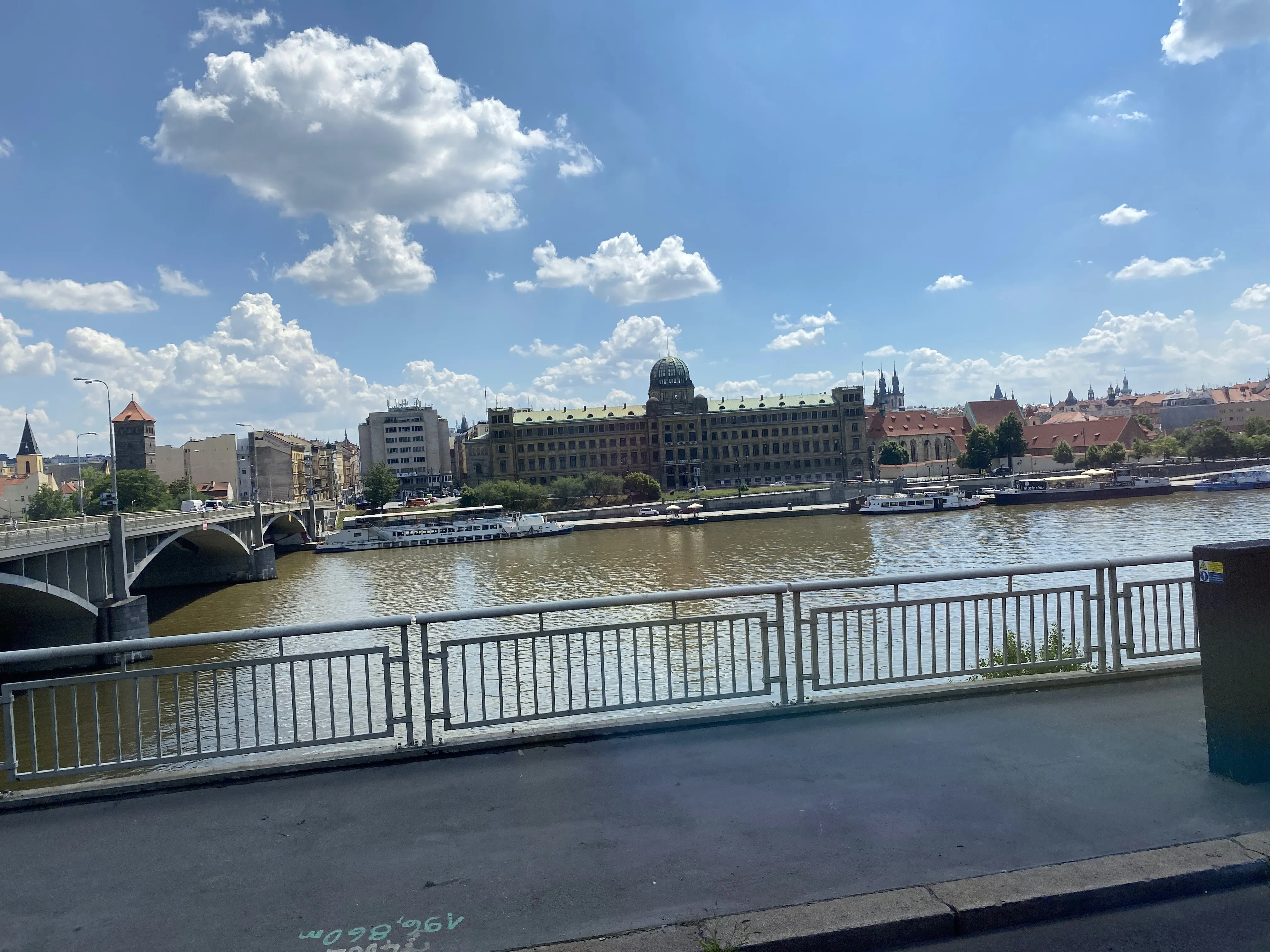 A scenic view of the Vltava River in Prague with historic buildings and bridges under a blue sky.