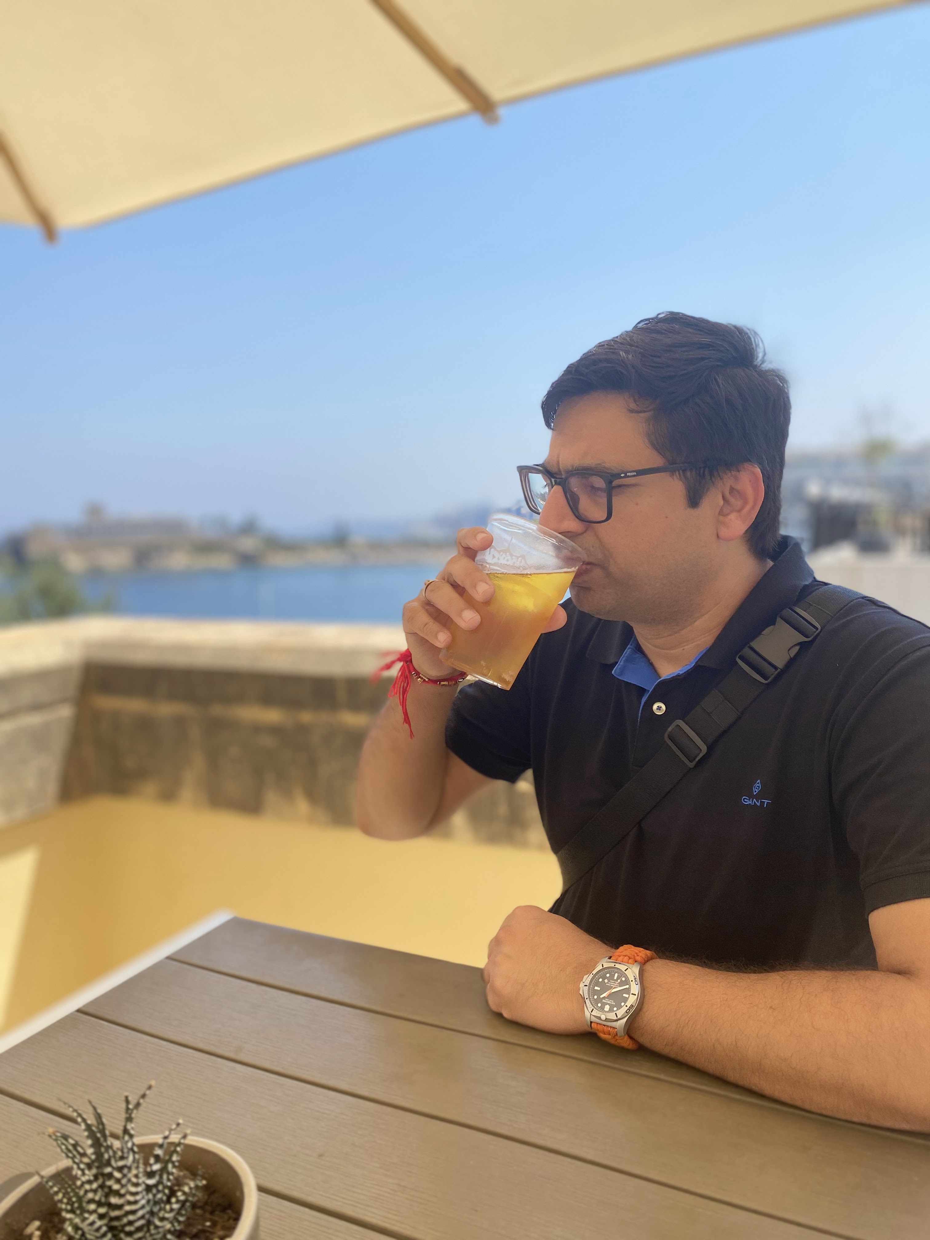 A man sipping a drink at an outdoor cafe with a scenic view of the sea in Malta.